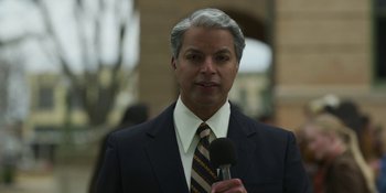 Movie still from “Love & Death” (2023), directed by Clark Johnson – A man in a suit and tie holding a microphone; Close Up shot, Low angle