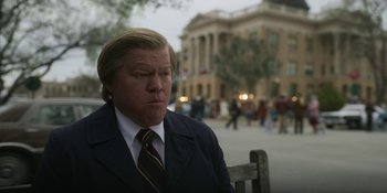 Movie still from “Love & Death” (2023), directed by Clark Johnson – A man sitting on top of a wooden bench outside; Medium shot, Low angle
