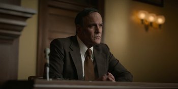 Movie still from “Love & Death” (2023), directed by Clark Johnson – A man in a suit and tie sitting in front of a table; Close Up shot, Low angle