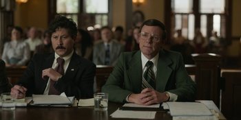 Movie still from “Love & Death” (2023), directed by Clark Johnson – Two men sitting at a table in front of other people; Medium shot, Low angle