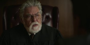 Movie still from “Love & Death” (2023), directed by Clark Johnson – An older man in a black robe and a white beard; Close Up shot, High angle