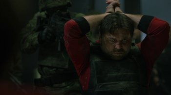 Movie still from “Money Heist” (2017), created by Álex Pina – A man in a black and red outfit holding his hands up; Close Up shot, Over the shoulder angle