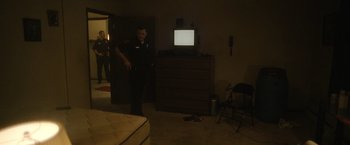 Movie still from “Monster” (2022), directed by Clement Virgo – A man standing in front of a television in a room; Wide shot, High angle