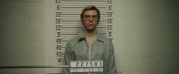 Movie still from “Monster” (2022), directed by Clement Virgo – A man in a gray shirt is in front of a police line - up; Medium shot, Low angle