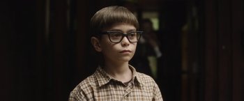 Movie still from “Monster” (2022), directed by Clement Virgo – A young boy wearing glasses and a plaid shirt; Close Up shot, High angle