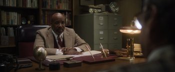 Movie still from “Monster” (2022), directed by Clement Virgo – A man sitting at a desk in front of papers; Medium shot, High angle