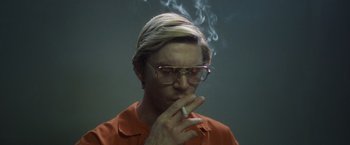 Movie still from “Monster” (2022), directed by Clement Virgo – A man with glasses is smoking a cigarette in front of a green wall; Close Up shot, Low angle