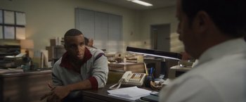 Movie still from “Monster” (2022), directed by Clement Virgo – A man sitting at a desk in front of a phone; Medium shot, Over the shoulder angle