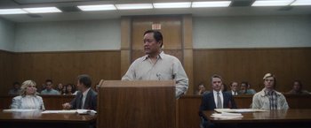 Movie still from “Monster” (2022), directed by Clement Virgo – A man standing in front of a podium in a courtroom; Medium shot, Low angle