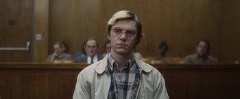 Movie still from “Monster” (2022), directed by Clement Virgo – A man with blonde hair and glasses in front of a group of people in a court room; Medium shot, Low angle