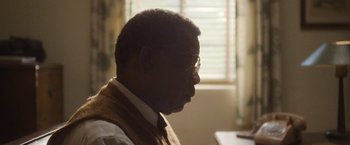 Movie still from “Monster” (2022), directed by Clement Virgo – A person wearing glasses and a vest; Close Up shot, Over the shoulder angle