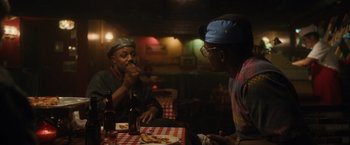 Movie still from “Monster” (2022), directed by Clement Virgo – Two men sitting at a table in front of plates of food; Medium shot, Over the shoulder angle