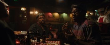 Movie still from “Monster” (2022), directed by Clement Virgo – Two men sitting at a table in front of drinks; Medium shot, Over the shoulder angle