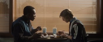 Movie still from “Monster” (2022), directed by Clement Virgo – Two men sitting at a table eating food; Medium shot, Over the shoulder angle