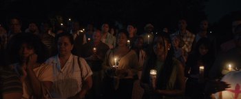 Movie still from “Monster” (2022), directed by Clement Virgo – A group of people holding lit candles at night; Wide shot, High angle