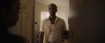 Movie still from “Monster” (2022), directed by Clement Virgo – A man standing in front of a door in a room; Medium shot, Low angle