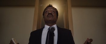Movie still from “Monster” (2022), directed by Clement Virgo – A man in a suit and tie looking upward; Close Up shot, Low angle