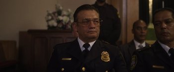 Movie still from “Monster” (2022), directed by Clement Virgo – A man in a police uniform sitting in front of flowers; Close Up shot, Low angle