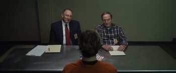 Movie still from “Monster” (2022), directed by Clement Virgo – Two men sitting at a table in front of another man; Medium shot, Over the shoulder angle