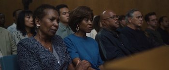 Movie still from “Monster” (2022), directed by Clement Virgo – A group of people sitting in front of a crowd; Medium shot, Low angle