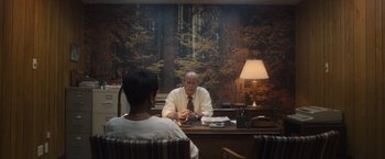 Movie still from “Monster” (2022), directed by Clement Virgo – A man sitting at a desk in front of a woman; Wide shot, Over the shoulder angle
