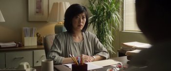 Movie still from “Monster” (2022), directed by Clement Virgo – A woman sitting at a table with papers and pencils in front of her; Medium shot, Over the shoulder angle