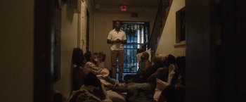 Movie still from “Monster” (2022), directed by Clement Virgo – A group of people sitting in a living room; Wide shot, Low angle