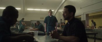 Movie still from “Monster” (2022), directed by Clement Virgo – A man standing in front of other men in a room; Medium shot, Over the shoulder angle
