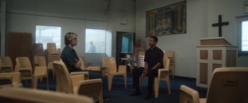 Movie still from “Monster” (2022), directed by Clement Virgo – Two men are sitting in chairs in a room; Wide shot, Over the shoulder angle