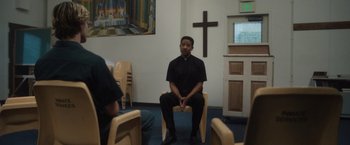 Movie still from “Monster” (2022), directed by Clement Virgo – A man sitting on a chair in a room; Wide shot, Over the shoulder angle