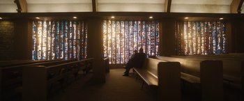 Movie still from “Monster” (2022), directed by Clement Virgo – A man sitting on a bench in front of a stained glass window; Extreme Wide shot, Low angle
