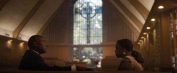 Movie still from “Monster” (2022), directed by Clement Virgo – A woman sitting in front of a stained - glass window; Wide shot, Low angle