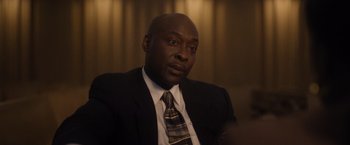 Movie still from “Monster” (2022), directed by Clement Virgo – A man wearing a suit and tie sitting in a room; Close Up shot, High angle