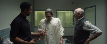 Movie still from “Monster” (2022), directed by Clement Virgo – A man in a white robe is getting his hair cut by two other men; Medium shot, Over the shoulder angle