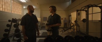 Movie still from “Monster” (2022), directed by Clement Virgo – Two men standing in a room with a gym in the background; Medium shot, Low angle