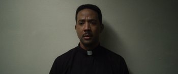 Movie still from “Monster” (2022), directed by Clement Virgo – A man wearing a black shirt and a white collar; Close Up shot, Low angle