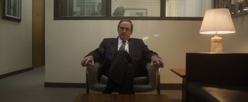 Movie still from “Monster” (2022), directed by Clement Virgo – An older man in a suit and tie sitting in a chair in an office setting; Medium shot, Low angle