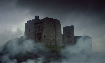 Movie still from “Monty Python and the Holy Grail” (1975), directed by Terry Gilliam – A castle is surrounded by a cloud filled sky; Extreme Wide shot, Low angle