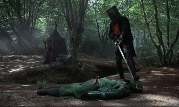 Movie still from “Monty Python and the Holy Grail” (1975), directed by Terry Gilliam – A man in a costume standing next to a dead body in the woods; Wide shot, High angle