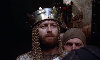 Movie still from “Monty Python and the Holy Grail” (1975), directed by Terry Gilliam – A man wearing a crown and a chain mail outfit; Close Up shot, Low angle