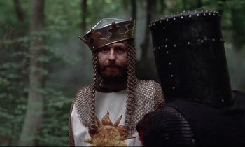 Movie still from “Monty Python and the Holy Grail” (1975), directed by Terry Gilliam – A man wearing a helmet and a chain mail armor; Medium shot, Over the shoulder angle