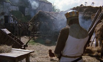 Movie still from “Monty Python and the Holy Grail” (1975), directed by Terry Gilliam – A man wearing a chain mail armor and holding a chicken in his hand; Wide shot, High angle