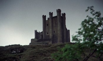 Movie still from “Monty Python and the Holy Grail” (1975), directed by Terry Gilliam – A castle on top of a hill with trees in the background; Extreme Wide shot, Low angle