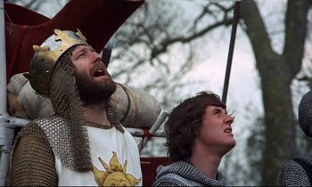 Movie still from “Monty Python and the Holy Grail” (1975), directed by Terry Gilliam – Two men dressed in medieval clothing and one is holding an umbreall; Medium shot, Low angle