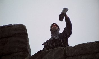 Movie still from “Monty Python and the Holy Grail” (1975), directed by Terry Gilliam – A man dressed as a medieval knight holding a sword; Medium shot, Low angle