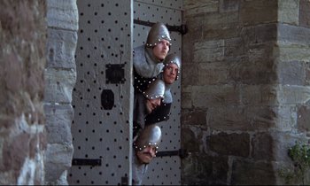 Movie still from “Monty Python and the Holy Grail” (1975), directed by Terry Gilliam – Two people dressed in medieval costumes are peeking out of a door way; Wide shot, High angle