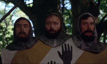 Movie still from “Monty Python and the Holy Grail” (1975), directed by Terry Gilliam – A group of men in medieval costumes holding a sign; Medium shot, Low angle