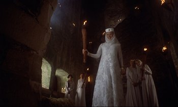 Movie still from “Monty Python and the Holy Grail” (1975), directed by Terry Gilliam – A woman in a white dress holding a torch; Wide shot, Low angle