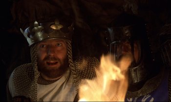 Movie still from “Monty Python and the Holy Grail” (1975), directed by Terry Gilliam – Two men in medieval garb are holding fire in a cave; Close Up shot, Low angle