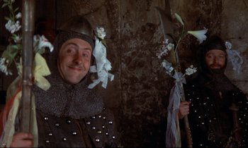 Movie still from “Monty Python and the Holy Grail” (1975), directed by Terry Gilliam – A man dressed as a medieval knight holding flowers; Medium shot, Low angle